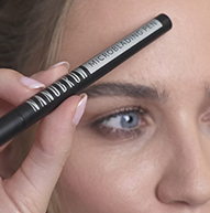 Modelka trzyma pióro Microblading blisko czoła