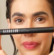 Modelka z czerwonymi ustami trzymająca poziomo tusz do rzęs Nanbrow Shape Mascara na twarzy