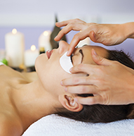 Osoba poddawana relaksującemu masażowi twarzy w spokojnym otoczeniu spa ze świecami w tle.