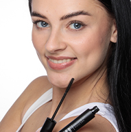 Uśmiechnięta modelka trzymająca aplikator tuszu do rzęs pod brodą